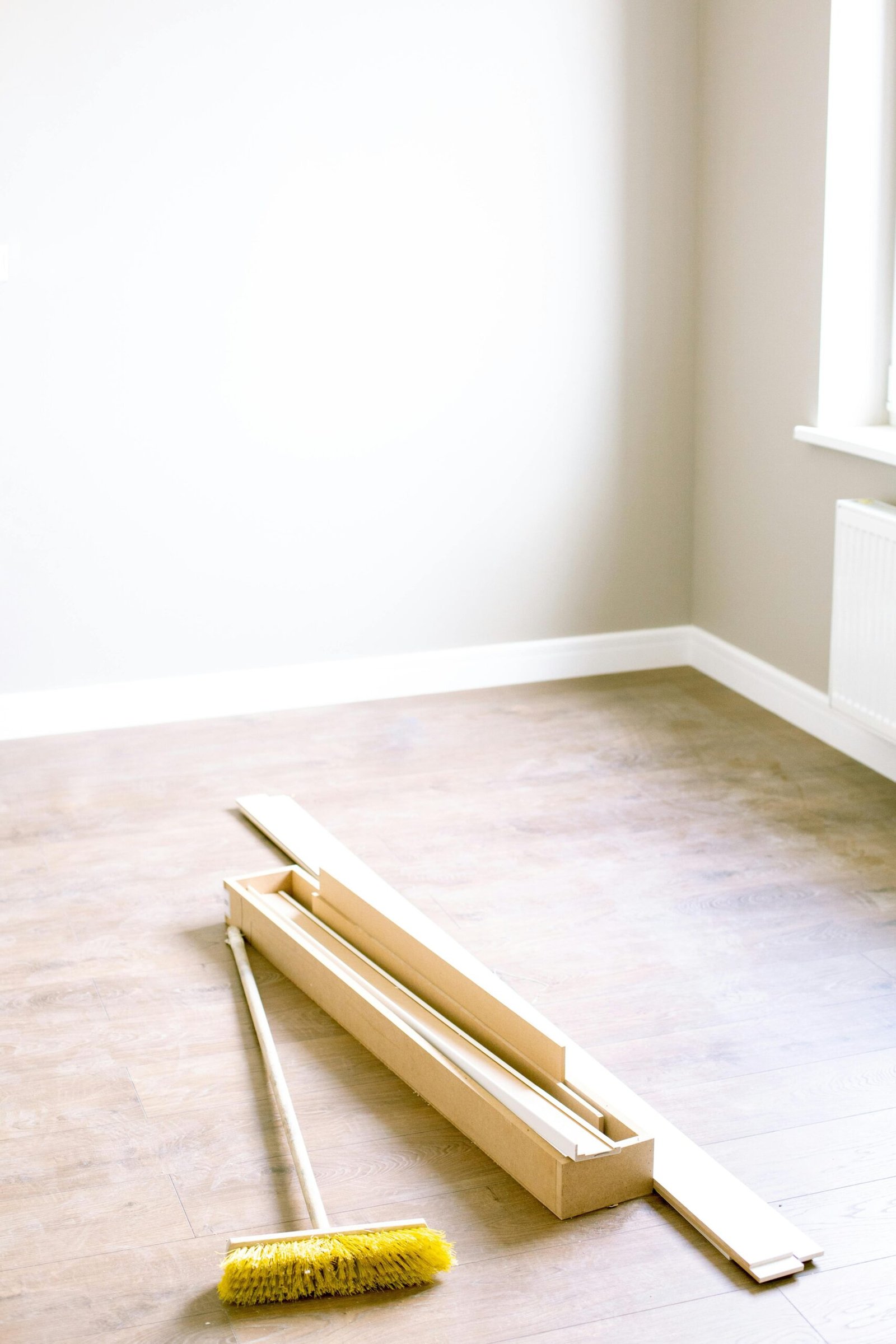 An empty room with wood planks and a broom, ready for renovation.